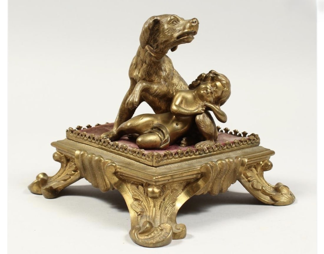 Gilt Bronze Dog and Sleeping Putto Figural Stand: Decorative gilt-bronze figural group depicting a seated hunting dog protectively posed beside a sleeping putto. The figures rest on a rose-colored velvet-covered platform above an ornate Rococo Reviva
