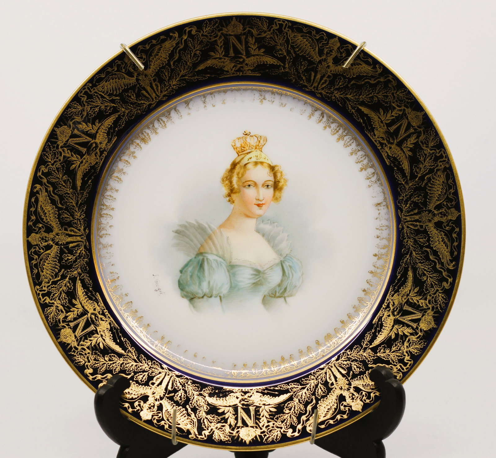 Sevres Style Porcelain Portrait Plate, C. 1805: French porcelain portrait plate depicting a crowned young woman in a pale blue dress, surrounded by a deep cobalt border richly decorated with gilt Napoleonic-style eagles, oak leaves, crowns, and rep