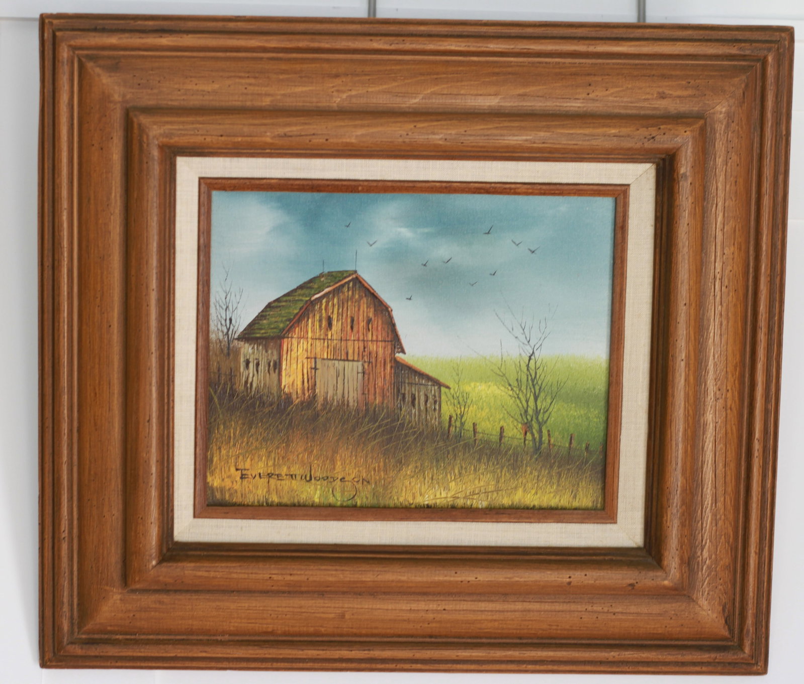 Everett Woodson, Rustic Barn Landscape, Oil on Canvas, Signed: An oil on canvas painting depicting a weathered wooden barn with a moss covered roof set within a golden field of tall grasses, birds in flight across a blue sky, and a wire fence lined with bare tree