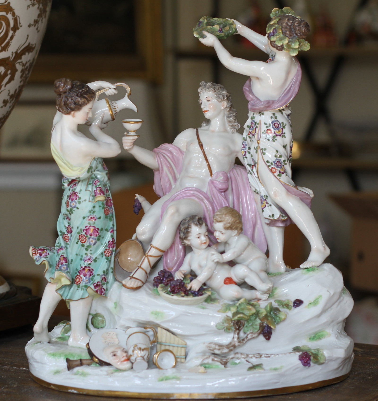 Large Antique Porcelain Bacchus and Attendants Figural Group: Large Continental porcelain figural group depicting Bacchus seated with attendants, putti, grapes, and a reclining leopard. Finely modeled with colorful hand painted floral decoration, gilt accents, a