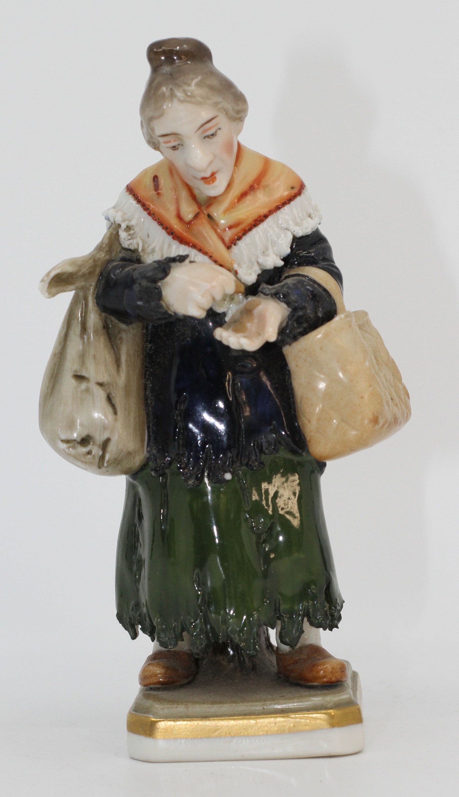 Capodimonte Porcelain Beggar Woman Figurine: Porcelain figurine depicting a woman carrying two bags and holding coins. Hand painted in naturalistic colors. Crown N mark to base.