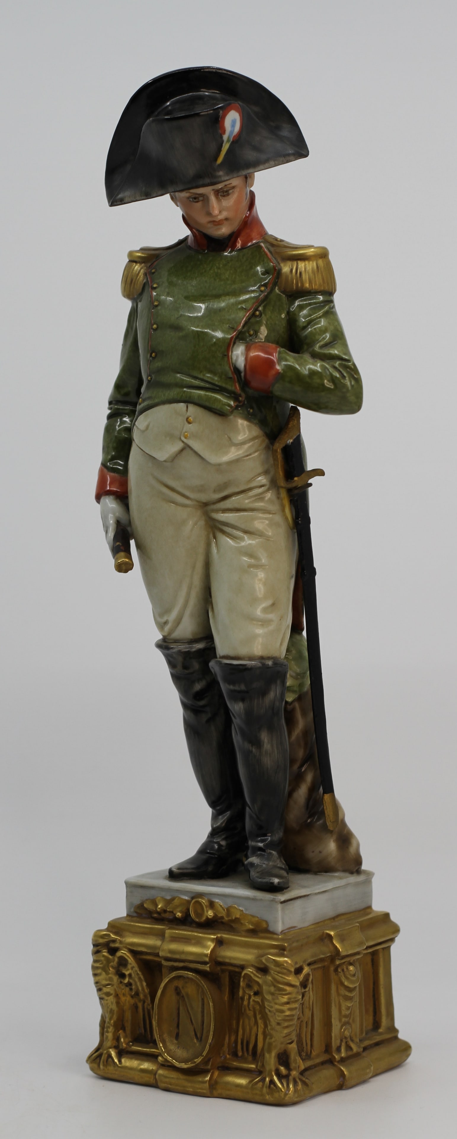 Capodimonte Porcelain Napoleonic Officer Figurine: Large porcelain figure of a Napoleonic officer wearing a green military coat, bicorne hat, white trousers, and tall black boots, holding a pistol and sword. Raised on an ornate gilt architectural