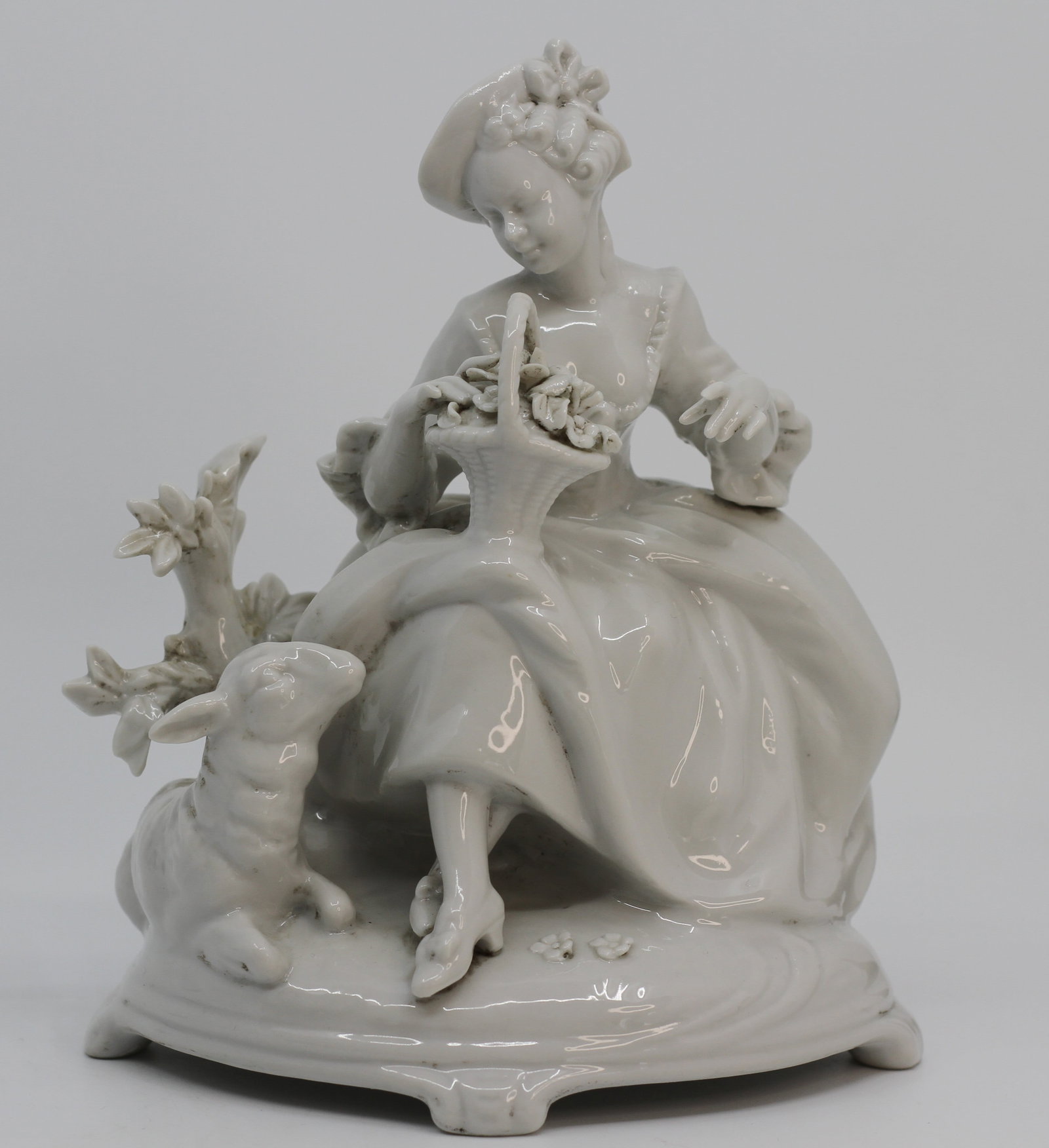 Ernst Bohne German Porcelain Lady with Dog Figurine: Early 20th century German porcelain figural group by Ernst Bohne Sohne depicting an elegant seated lady with flower basket and dog. White glazed porcelain with detailed floral and naturalistic element