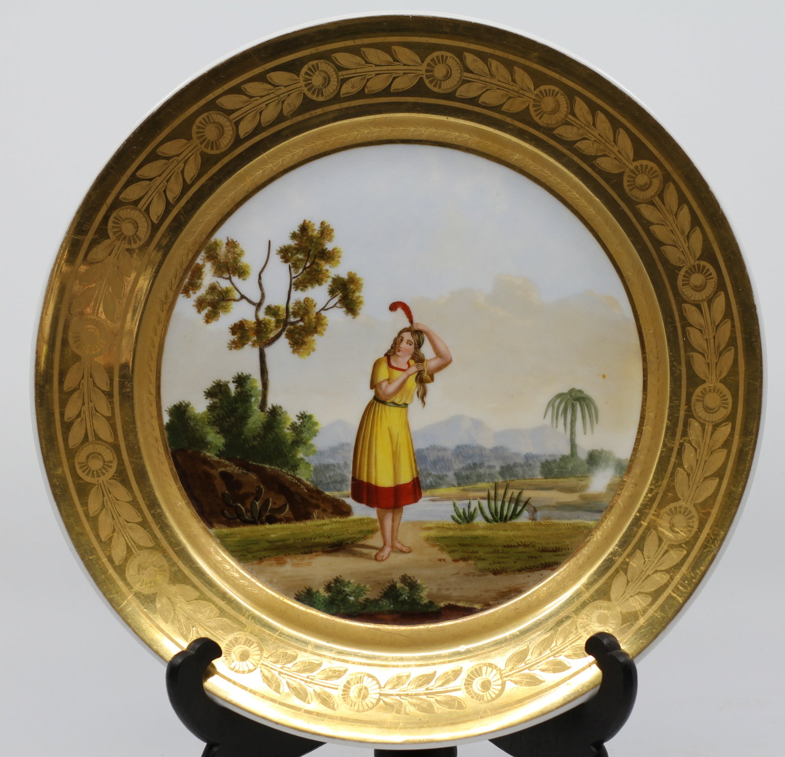 Denuelle Paris Porcelain Cabinet Plate, "Paysanne du Perou," Costume Study: A French porcelain cabinet plate retailed by Denuelle, Rue de Crussol, Paris, the center finely hand-painted with a full-length figure of a young woman in a yellow dress with red trim and a red-feathe