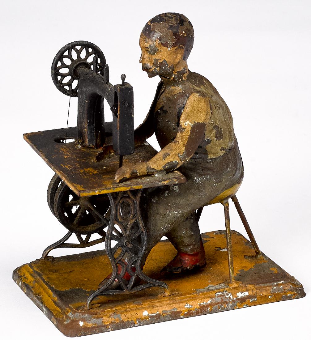 Carette painted tin tailor steam toy accessory: Carette painted tin tailor steam toy accessory, seated at a sewing machine, 6 1/4'' h. Provenance: Morton A. Hirschberg Steam Toy Collection.