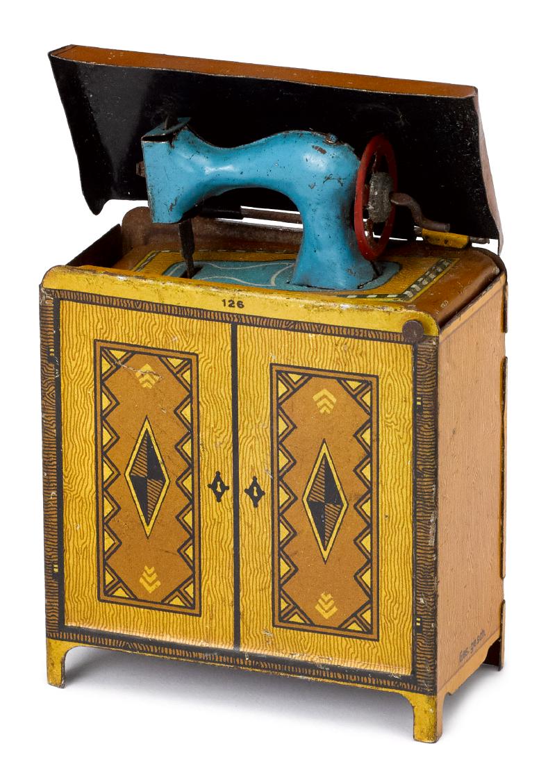 Scarce sewing machine cabinet penny toy: Scarce tin lithograph sewing machine cabinet penny toy, the machine drops down into a cabinet, hand crank on wheel of machine, 3 1/2'' h.