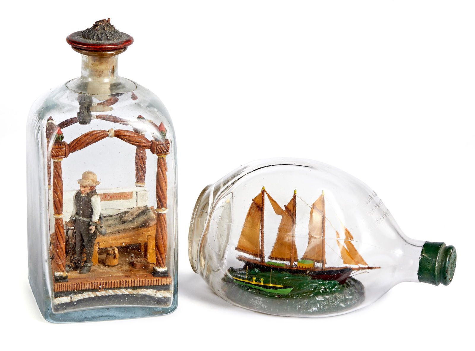 Two carved dioramas in bottles: Two carved dioramas in bottles, to include one of a man in chains standing next to a bed, overall height - 8'' and a sailship in a bottle, 7 3/4'' l.