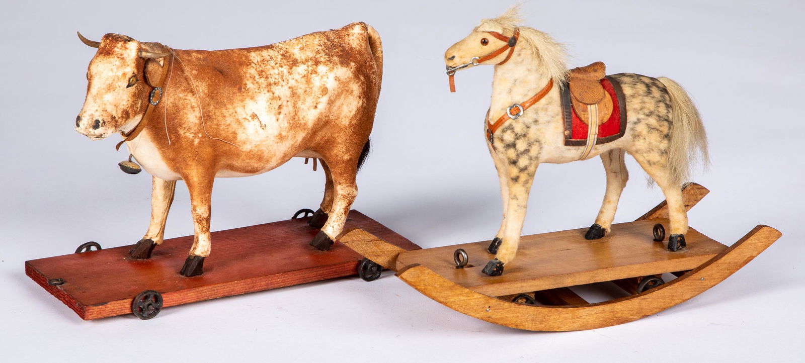Two composition animal pull toys: Two composition animal pull toys, to include a cow on a platform, 7 3/4'' l. and a dappled rocking horse, 8 3/4'' l.
