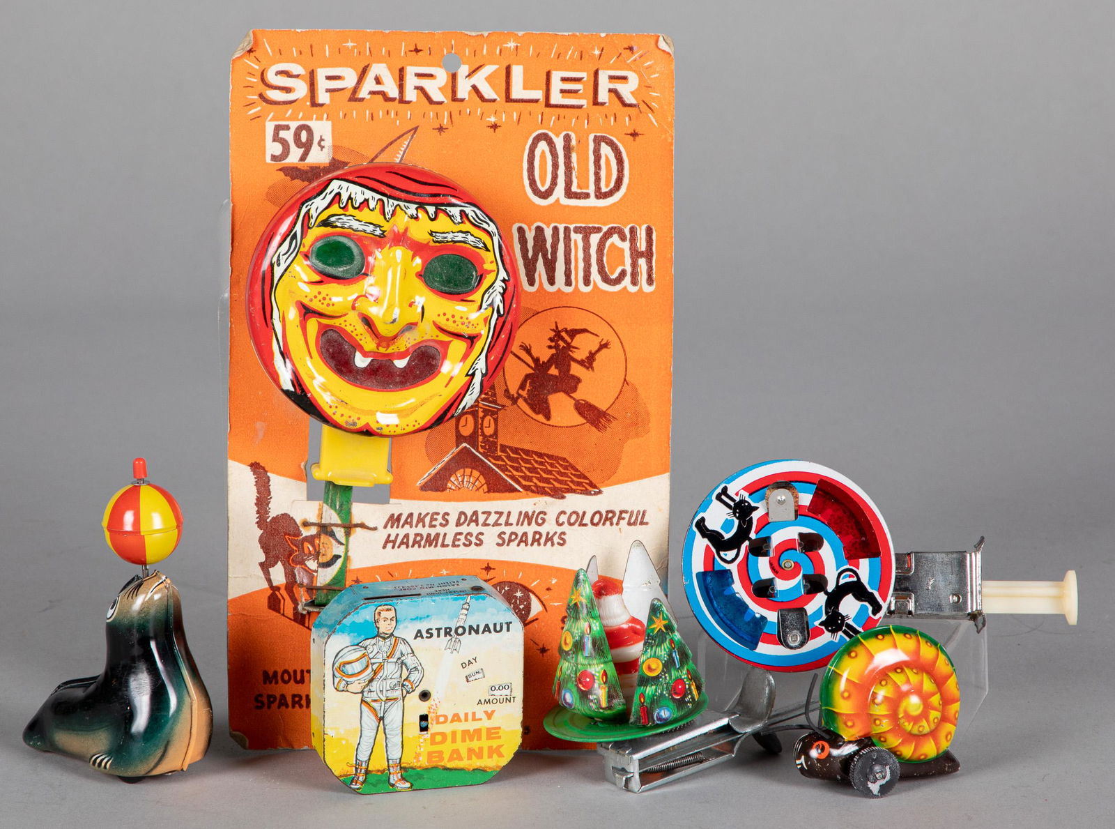 Group of tin lithograph sparkler toys, etc.: Group of tin lithograph sparkler toys, to include an Old Witch on original card, together with a tin Astronaut dime bank, a Lehmann wind-up snail and a seal.