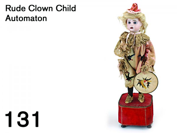 Rude Clown Child Automaton: a bisque head child in fanciful clown suit with running black geese appliqués on 2 color costume with elaborate lace trim, the only marking on head is an incised "4" on back of neck, he holds a hand 
