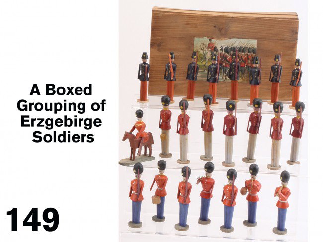 A Boxed Grouping of Erzgebirge Soldiers: a group of 23 painted wood Erzgebirge soldier in a wooden box with colorful illustrative paper label, includes 3 distinct styles of uniform - the 17 of the standing figures have rifles while 5 have mu