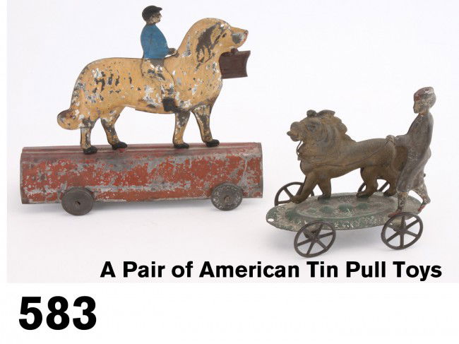 A Pair of American Tin Pull Toys: painted tin, includes boy with lion on embossed tin base with cast iron wheels, along with a boy riding dog on arched tin base with replaced tin wheels Size: larger 6.5" l.