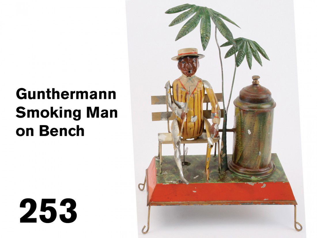 Gunthermann Smoking Man on Bench: painted tin with ingenious clockwork mechanism: the metal lid of the canister has a wire for holding a lit cigarette, a paper bellows housed beneath the enclosed smoke chamber pushes smoke through a t