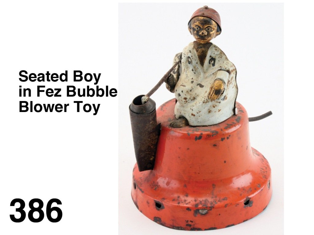 Seated Boy in Fez Bubble Blower Toy: painted tin and brass hand operated toy, depicts a robed boy with tasseled hat seated on a pedestal, with the press of a lever he dips his pipe in soap solution then raises pipe as if to mouth but air