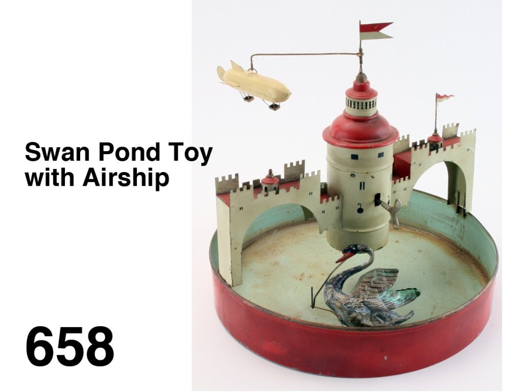 Swan Pond Toy with Airship: painted tin toy; pond is filled with water and when set in operation the swan swims around the central tower while the airship flies in circles, German manufacture Size: 13" diam., 12.5" t.