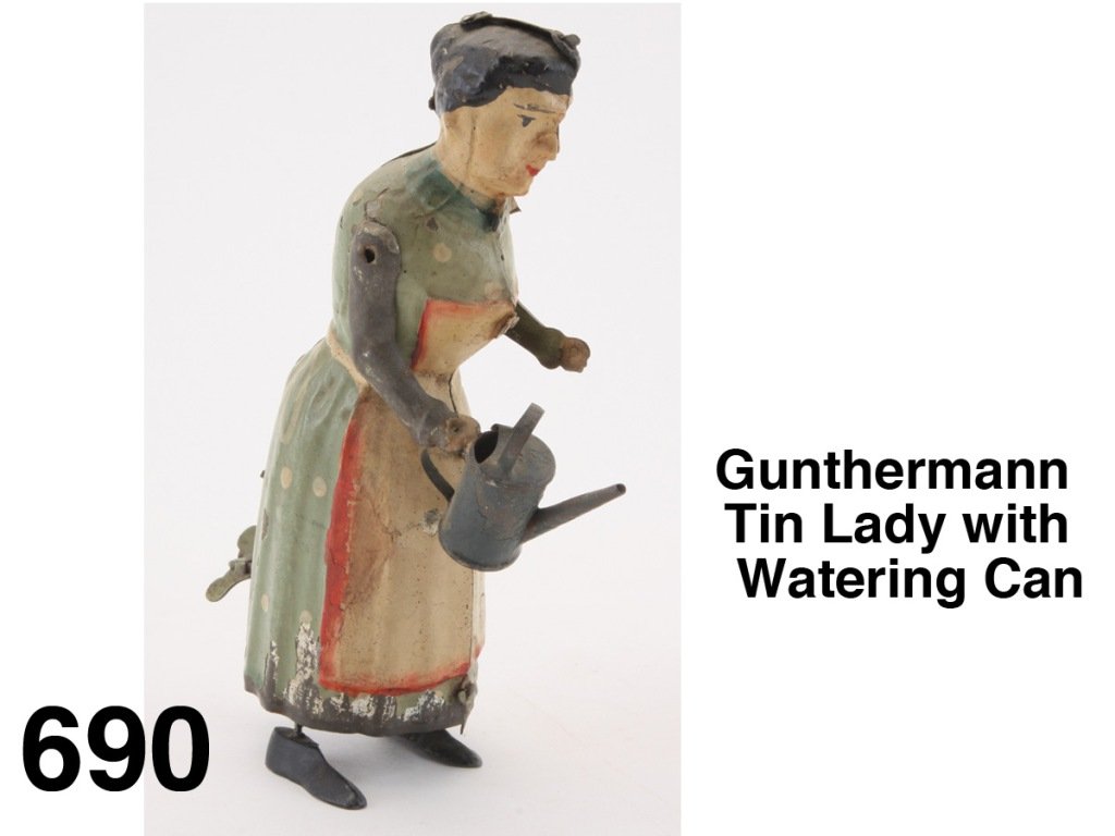 Gunthermann Tin Lady with Watering Can: painted tin figure with internal clockwork, a walking figure (slot in upper left shoulder area suggests she may have a carried a rake or other garden implement) Size: 7" t.