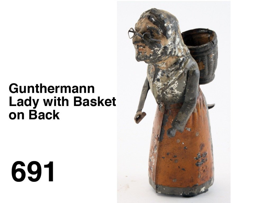 Gunthermann Lady with Basket on Back: painted tin with internal clockwork, she has realistically embossed tin basket on back and walks with a side to side gait Size: 6" t.