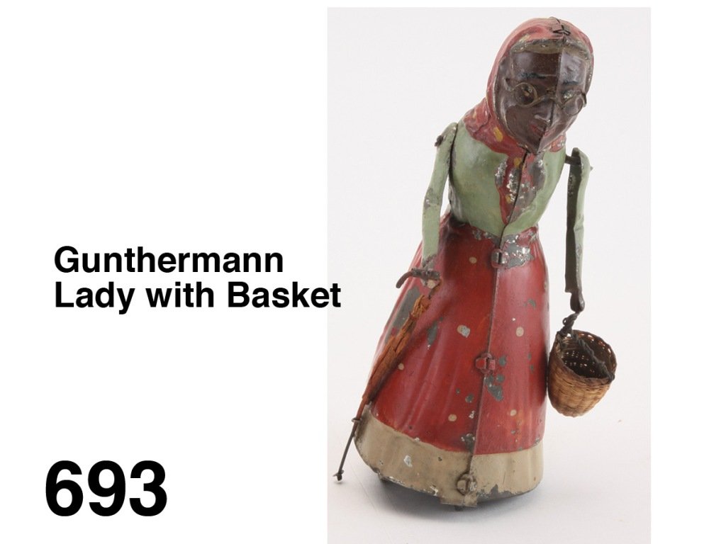 Gunthermann Lady with Basket: painted tin with internal clockwork, she holds basket and furled umbrella as she walks with a side to side gait Size: 7" t.