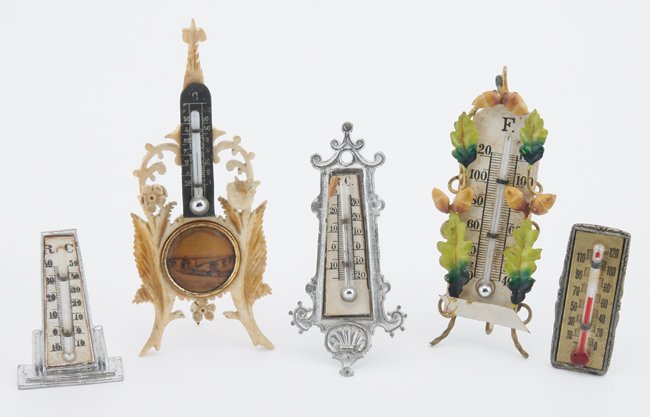 Five Miniature Thermometers: a collection as displayed by Mrs. Jacobs including 2 German pewter thermometers, an elaborately carved bone easel back with photographic image, a painted brass easel back with acorn leaves and nuts an