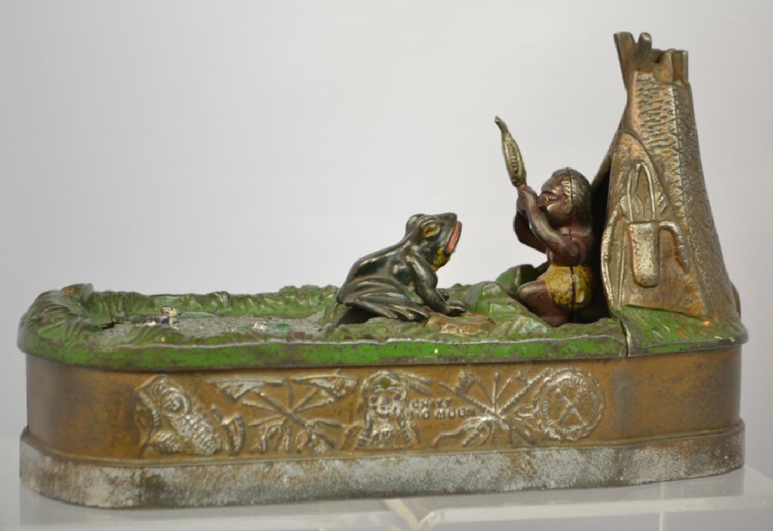 J. & E. Stevens Cast Iron Chief Big Moon Mechanica: J. & E. Stevens Cast Iron Chief Big Moon Mechanical Bank, circa 1899. Operates by lifting the pond platform, loading the frog into the pond, placing the coin into the coin slot (between the Indian and