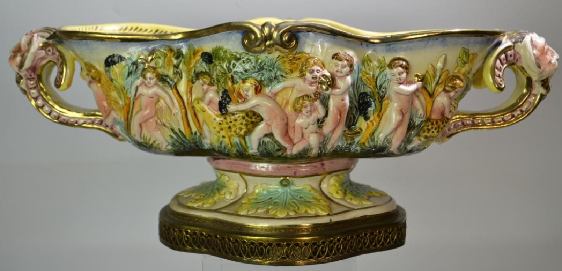 A 1940's Capodimonte Center Bowl: Item measures approx. 7 1/2"h x 19"w. It has figural handles and depicts putti playing with leopards. It has a reticulated brass brass and no visible damage.