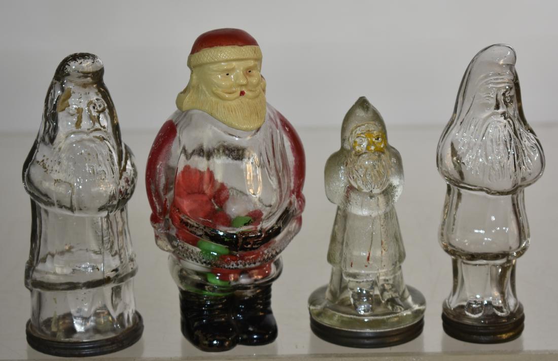 Four Vintage Glass Santa Candy Containers: Including a Santa with a plastic head measuring approx. 6"h with contents and original paper label. Also a German style Santa with a double cuff and original base cap, a Santa with a banded coat and o