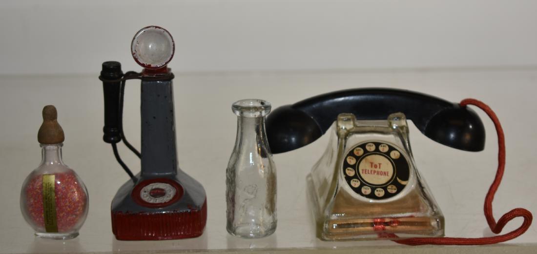 Four Vintage Glass Candy Containers: Including a "Lynne Type" telephone with a sunken dial, original paint and paper label. Also a "Tot:" telephone with a paper label, a "Stough's" nursing bottle with contents and a paper label and a "Do