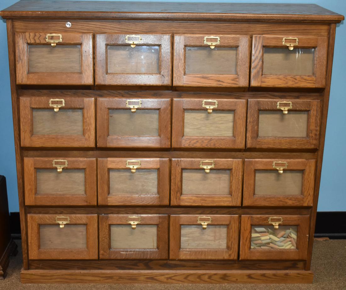 Sixteen Drawer Oak General Store Seed Cabinet: Item measures approx. 46"h x 51"w x 16"d. It is solid oak construction. It has sixteen bins with glass fronts, brass hardware and dates to the early 20th century.