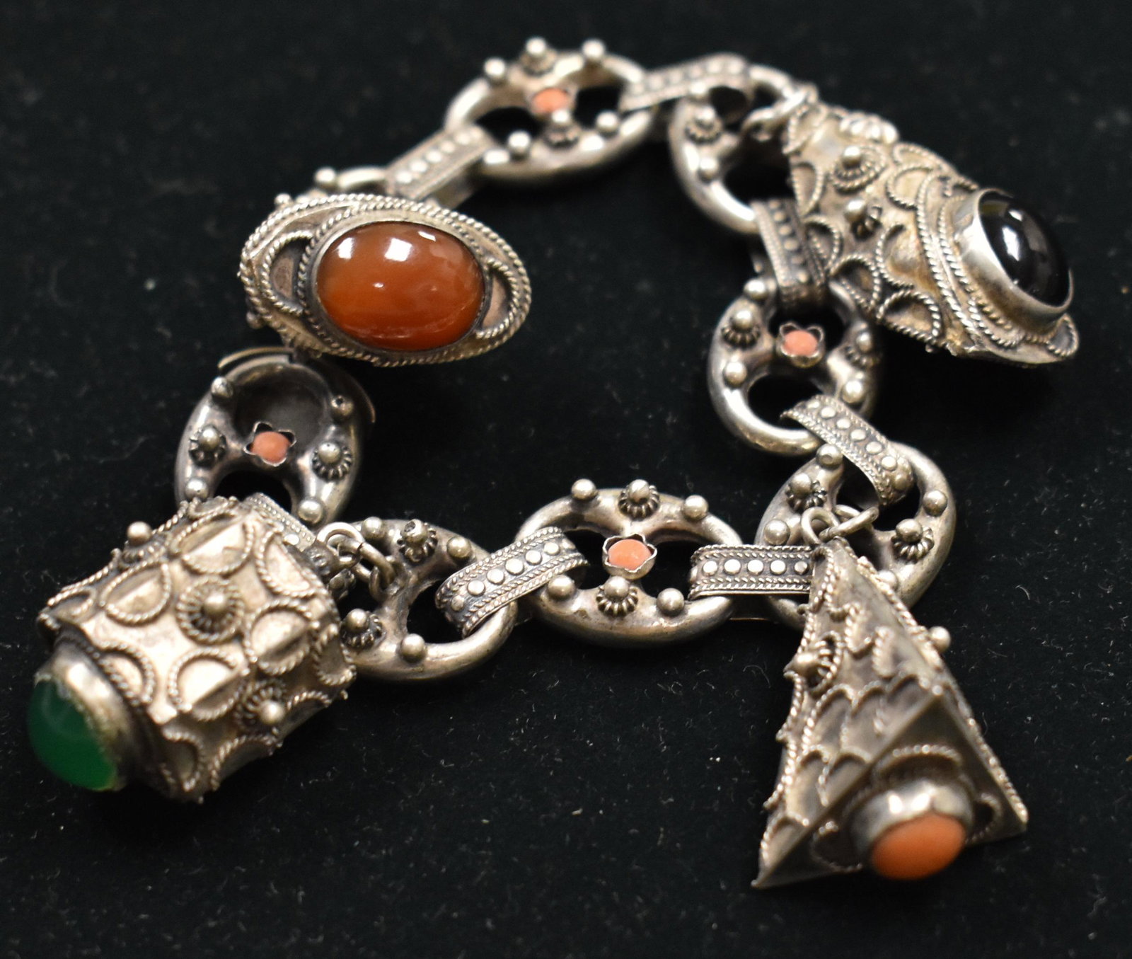 Ornate .800 silver Etruscan Charm Bracelet: The silver bracelet has angel skin coral, turquoise, carnelian and celadon set in charms. Note: A tiny piece of coral is missing.