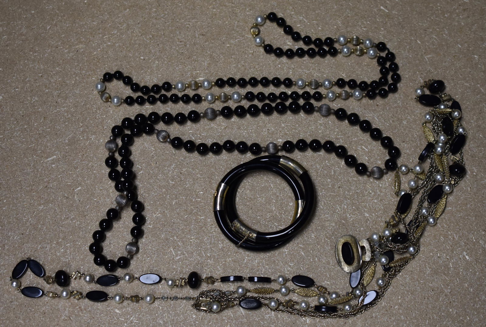 Onyx Jewelry Lot: includes vintage onyx, faux pearl and gold tone beads four stand necklace, one onyx and faux pearl necklace, one onyx bead and copper tone bead necklace, and two onyx bangles.
