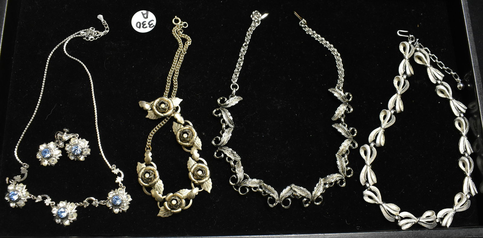 Four Silver Tone Necklaces: including one with blue and clear rhinestones and a pair of matching screwback earrings, a bow tie necklace, a leaf necklace, and a rose necklace.