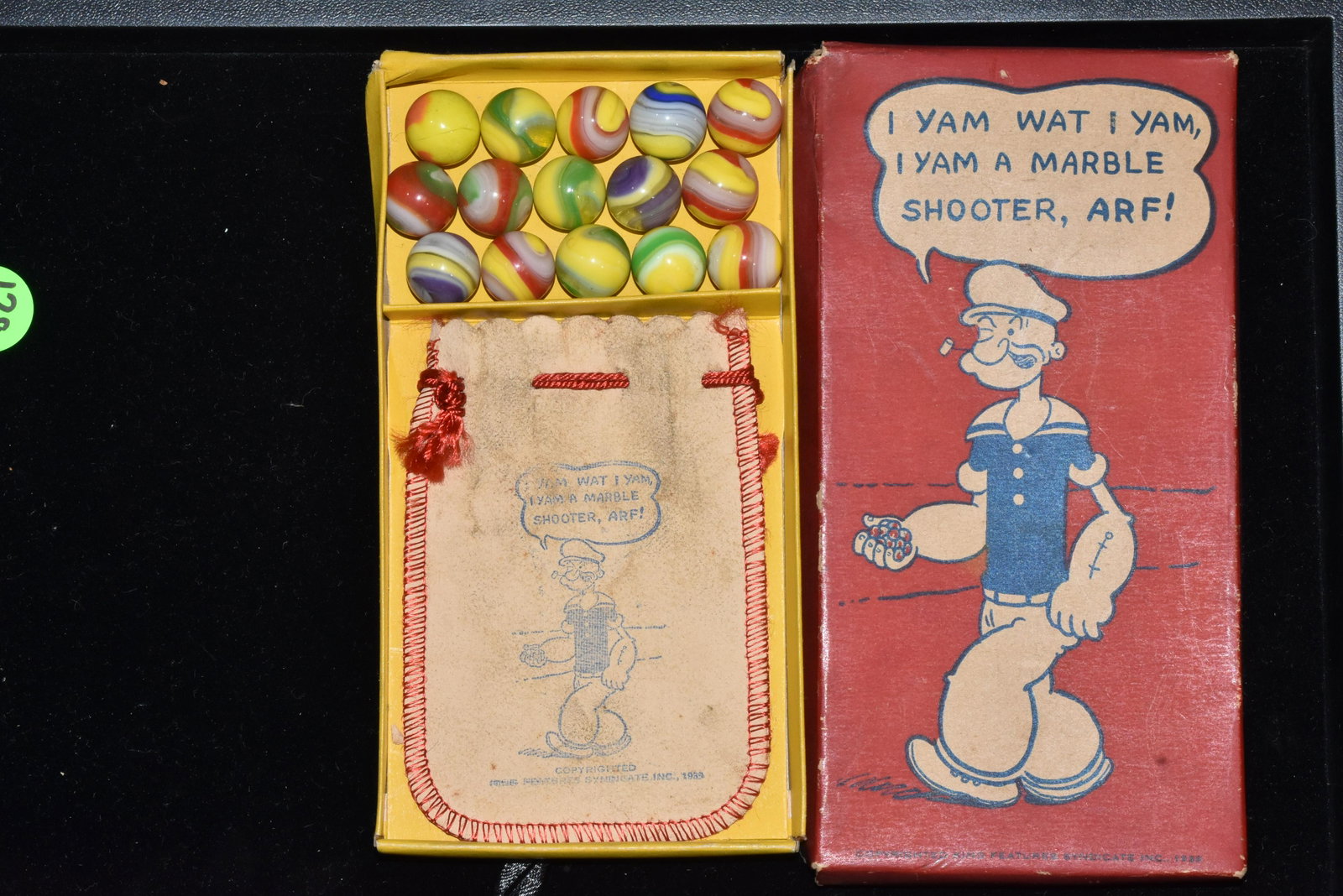 Akro Agate Popeye Marble Shooter Set in Box 1929: Box measures approx. 7" in length x 3 1/2"w.. Lid of box has a picture of Popeye and reads "I yam what I yam. I yam a marble shooter arf!". Below Popeye box reads copyright "King Features Syndicate, I