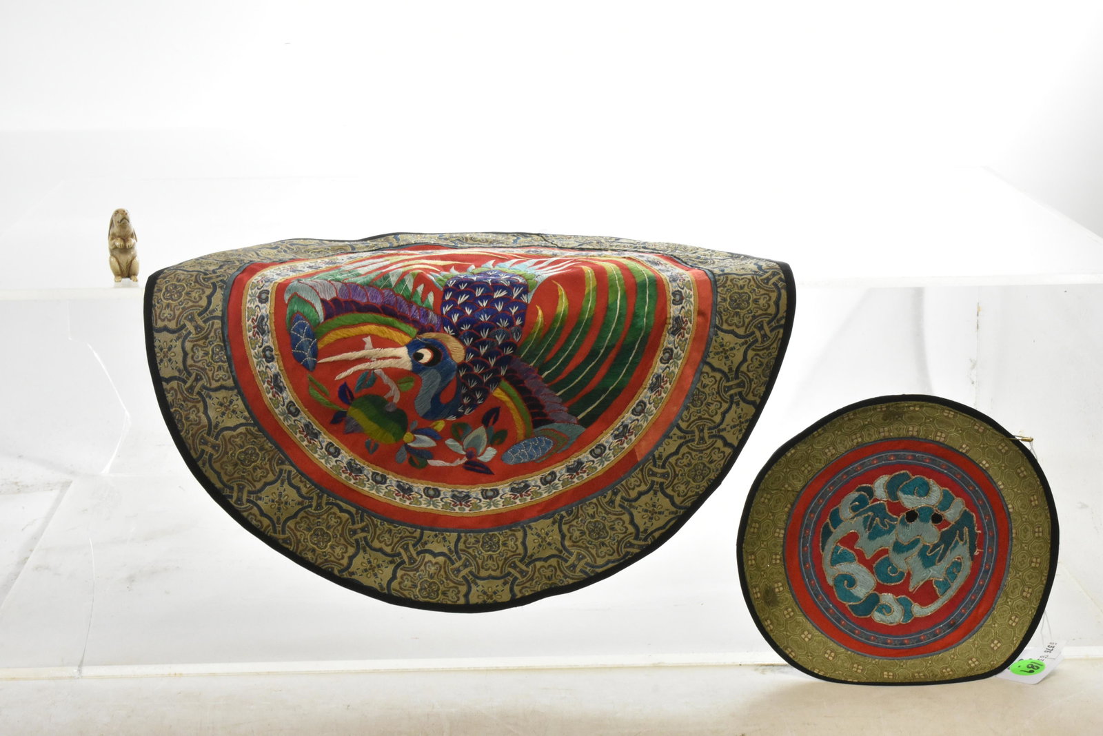 Two Ornate Asian Silk Table Throws: Larger measures approx. 14"dia. It depicts a peacock in the center with a floral border. It has a brown silk backing (backing has some staing near center that does not show through to front). Second m