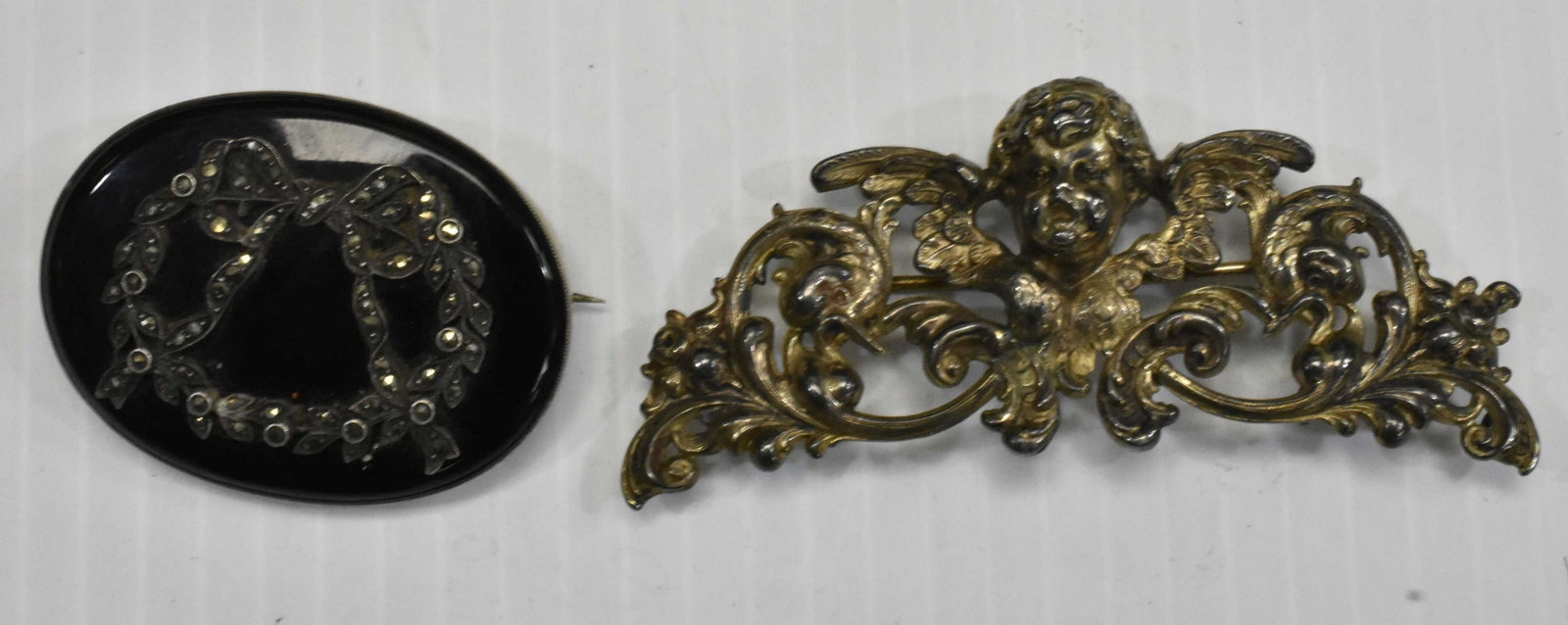 Two 19th Century Sterling Brooches: A signed "W. B. Kerr" chatelaine holder in the form of a cherub with a repousse floral design. Lot also includes an Edwardian sterling marcasite bow set in onyx. Black is approx 2 x 1 1/2" and chatela