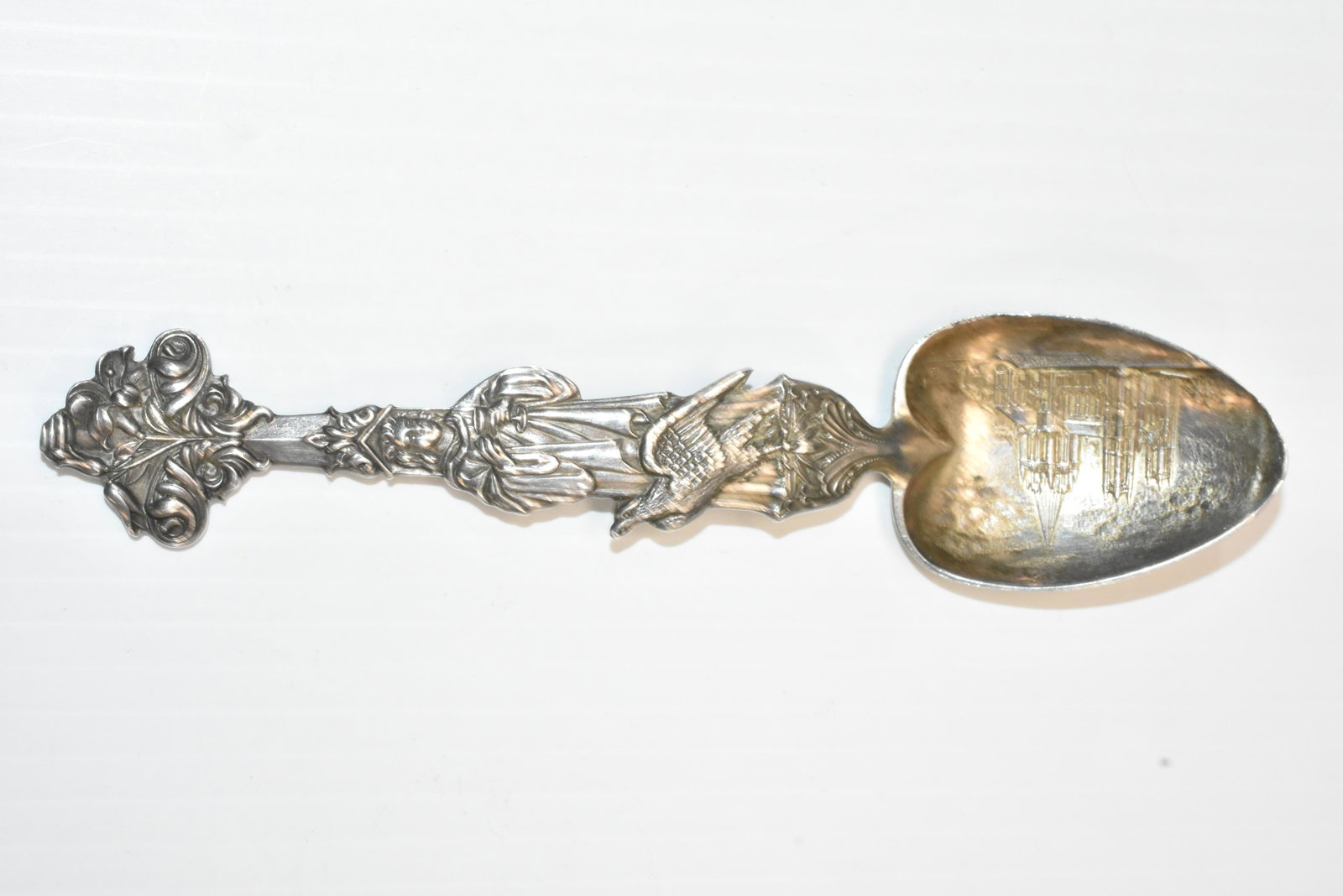 George Scheibler Ornate Sterling Spoon: Measures approx. 6" in length. It depicts a cathedral with a priest holding a chalice and an eagle at his feet. There is a Maltese cross on the back of the spoon bowl.