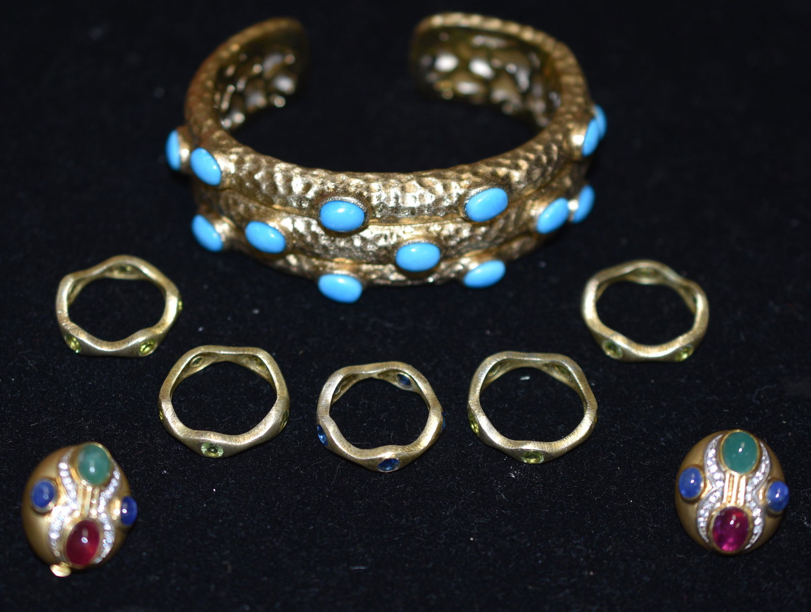 Modern Designer Jewelry Grouping: A large hammered cuff with blue stones, five stackable rings with stones and a pair of clip earrings with multi colored stones.