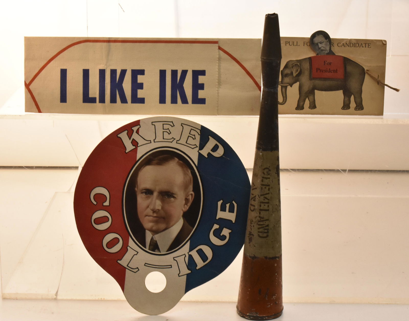 Vintage Political Collectibles: Lot includes a Cleveland and Stevenson megaphone, an "I Like Ike" cap, a Coolidge advertising fan, and a Cleveland pull for President card.