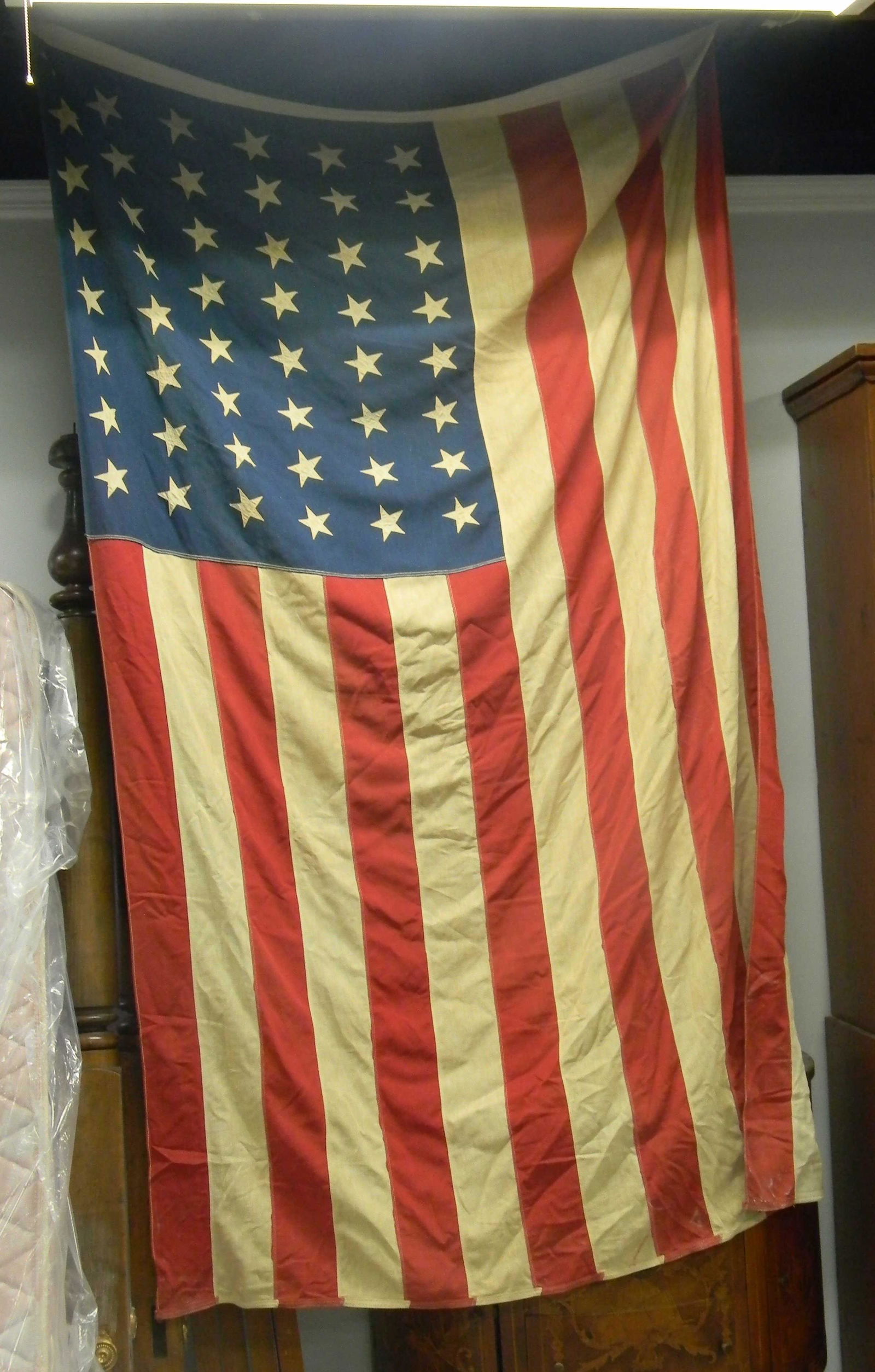 Large 48 Star American Flag: Item measures approximately 6'W x 8'L. It has applied stars, and woven stripes. It is a two-ply moth proof flag and it was produced by Defiance Company.