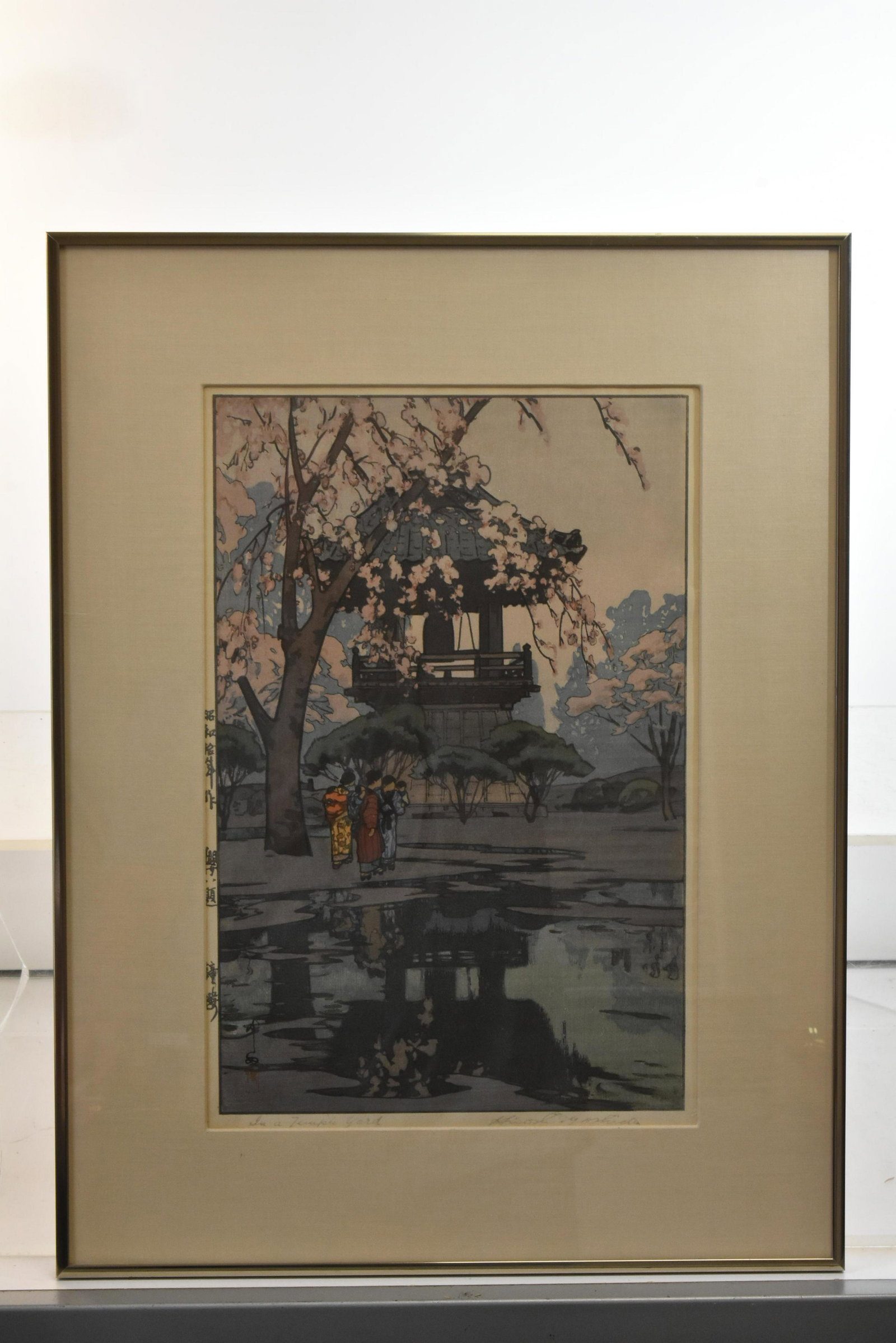 Hiroshige Yoshida Temple Scene: Exposed area measures approximately 15"H x 10"W. It depicts a Japanese temple with a cherry blossom tree, and ladies with children in front of a pond. It is titled "In a Temple Yard". It is hand signe