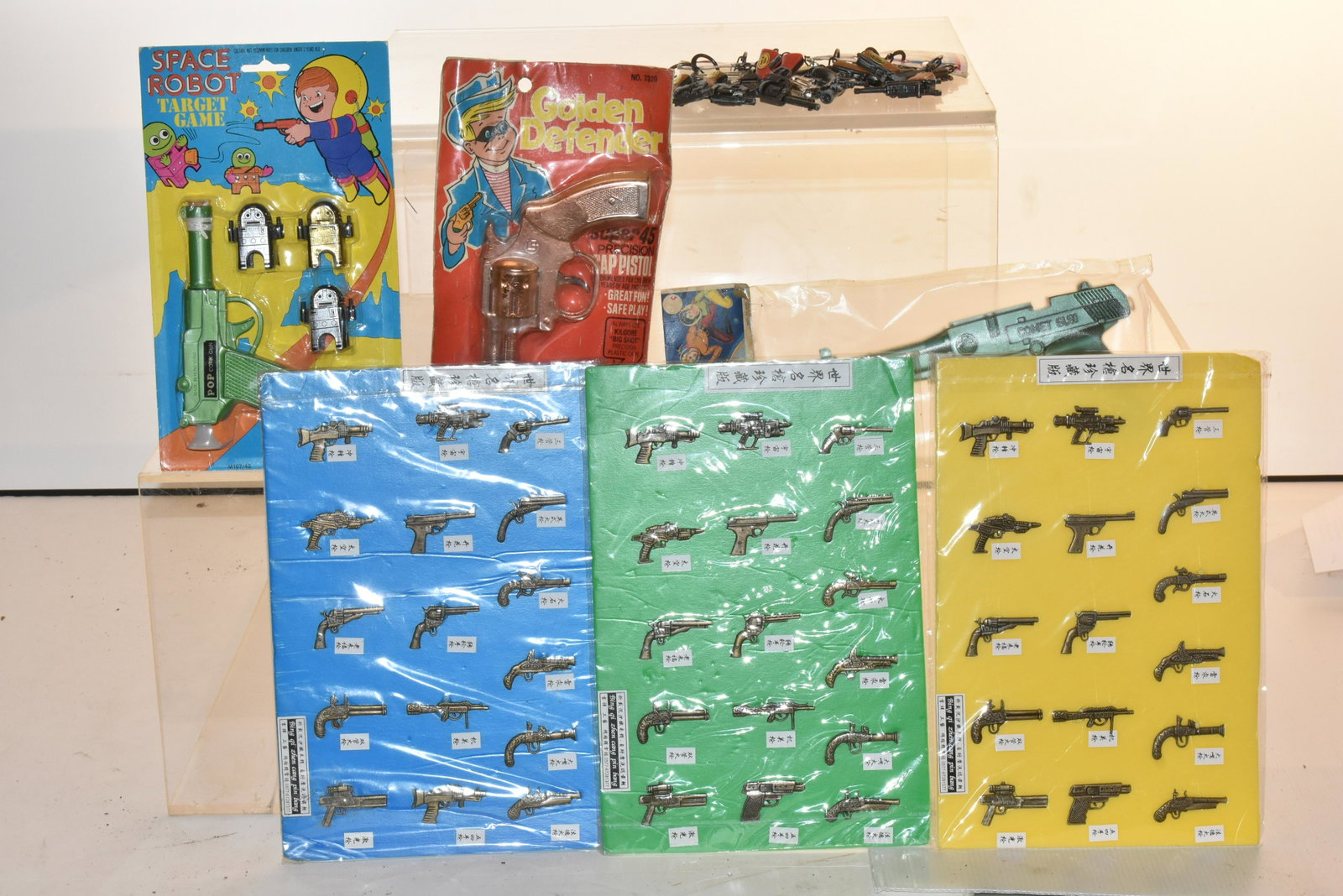 Toy Guns in Original Packs: Lot includes comic water pistol, die cast pistol key chains, golden defender cap pistol, space robot target game, and (3) sheets of Asian military weapon display figures.