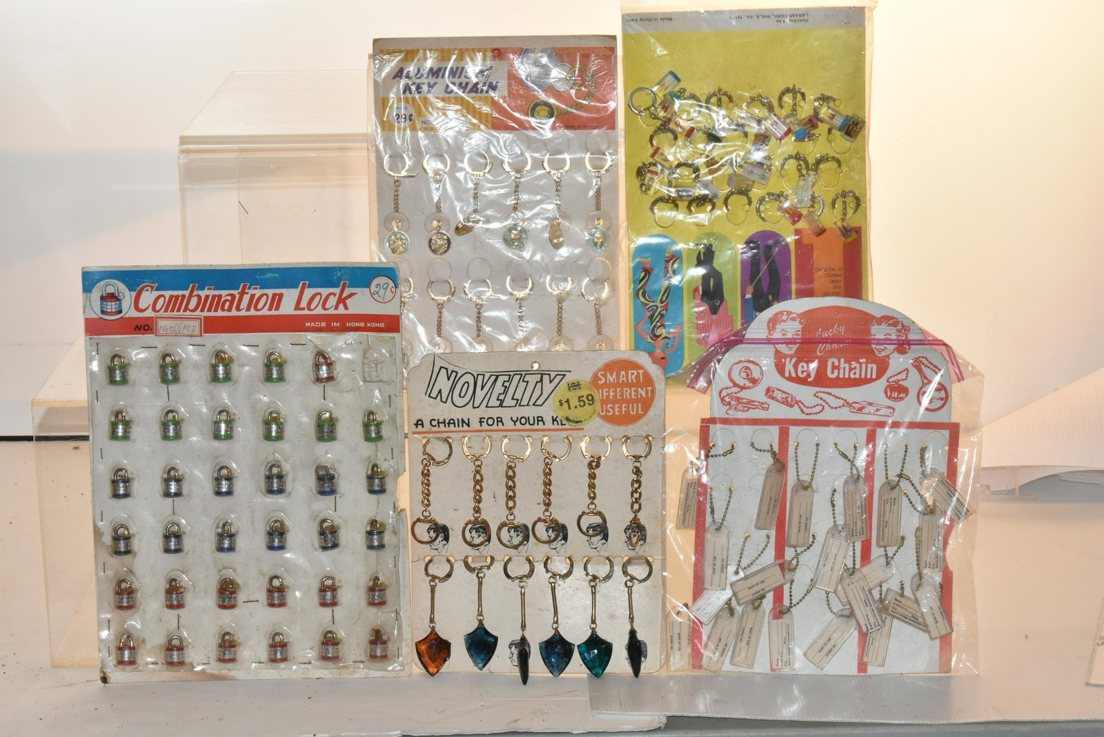 Toy Store Displays on Hang Cards: Lot includes artistic key rings from the 1970's, aluminum key chains, name and address key chains, novelty key chains with blue plastic arrowheads, and miniature combination locks. Most are complete o