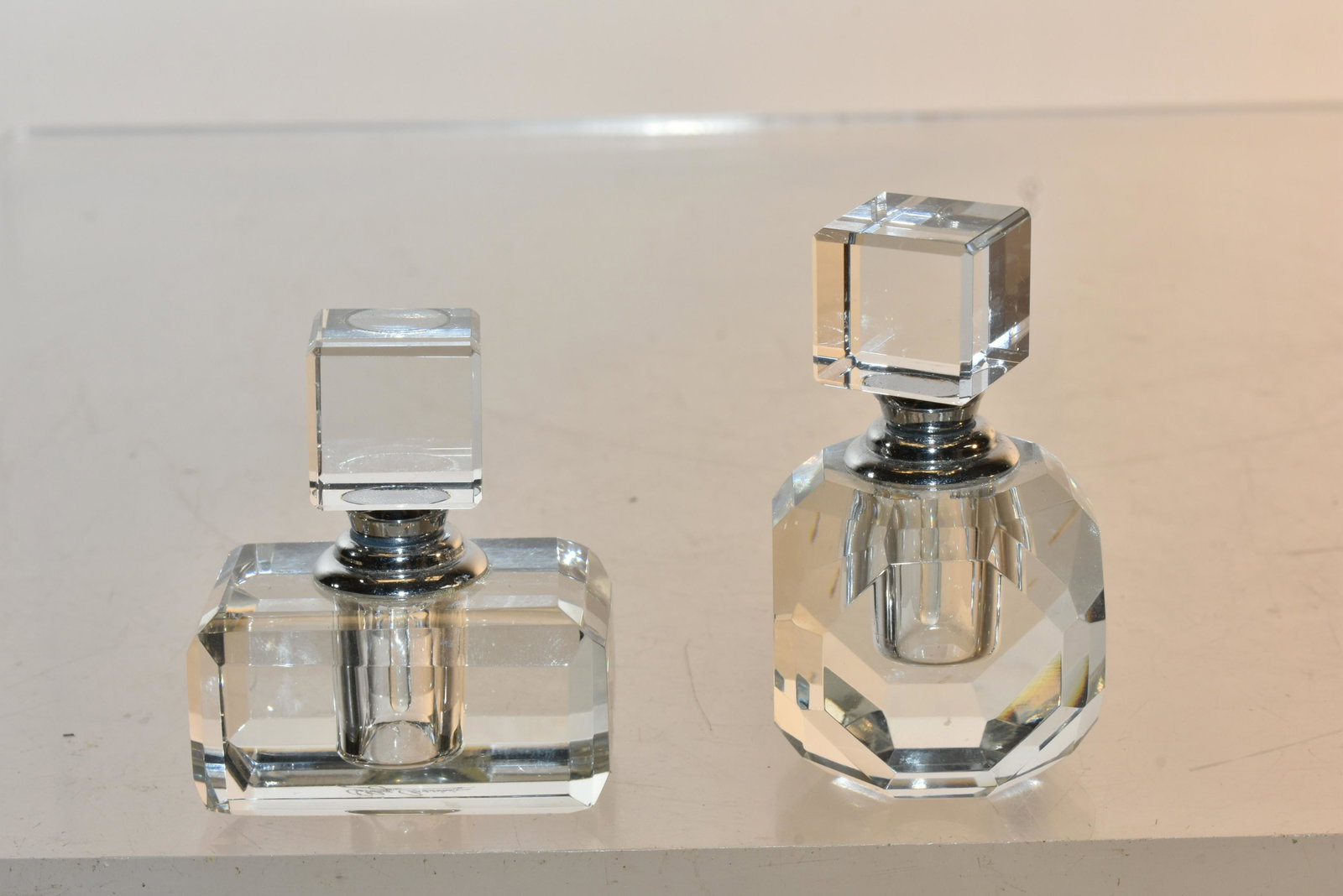 (2) Oleg Cassini Crystal Perfume Bottles: Largest item measures approximately 2.5"H. Both bottles are crystal with chrome mounts. Both are etched Oleg Cassini on bottom.