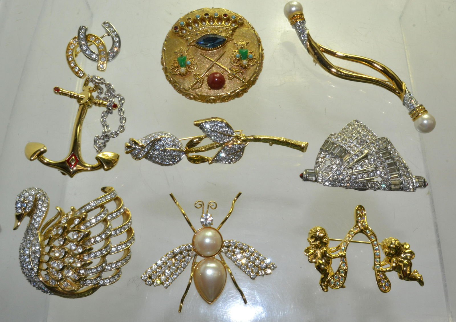 Vintage Designer Brooches: Lot includes a signed Bob Mackie anchor brooch, a Nolan Miller swan, a Kirk's Folly cherub, a Joan Rivers horseshoe, an Art brooch, and more.