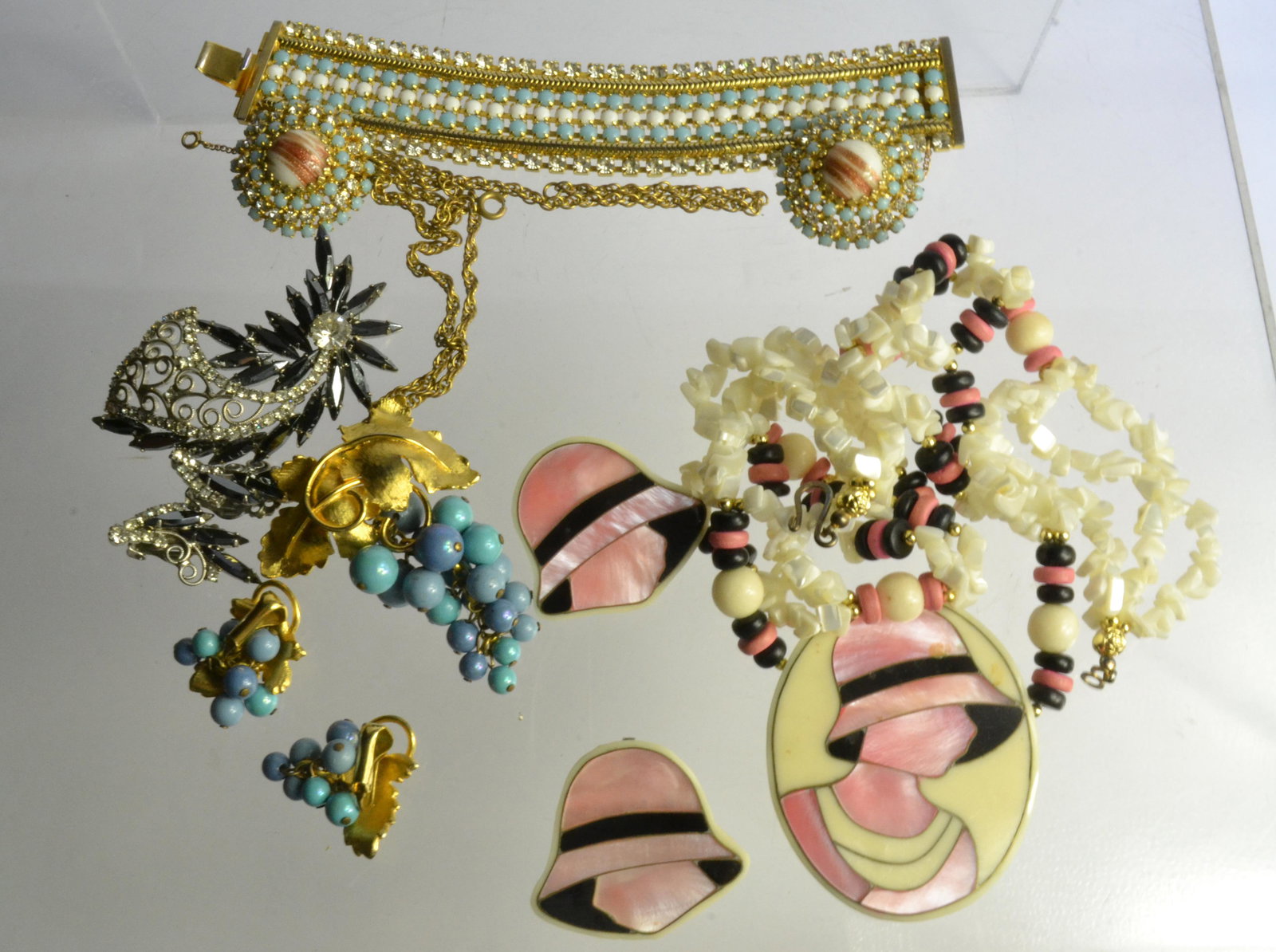 Vintage Hobe Jewelry and More: Lot includes a wide blue and white stone bracelet with matching clip earrings, signed Hobe, a large rhinestone brooch, and a seashell necklace with lady motif.