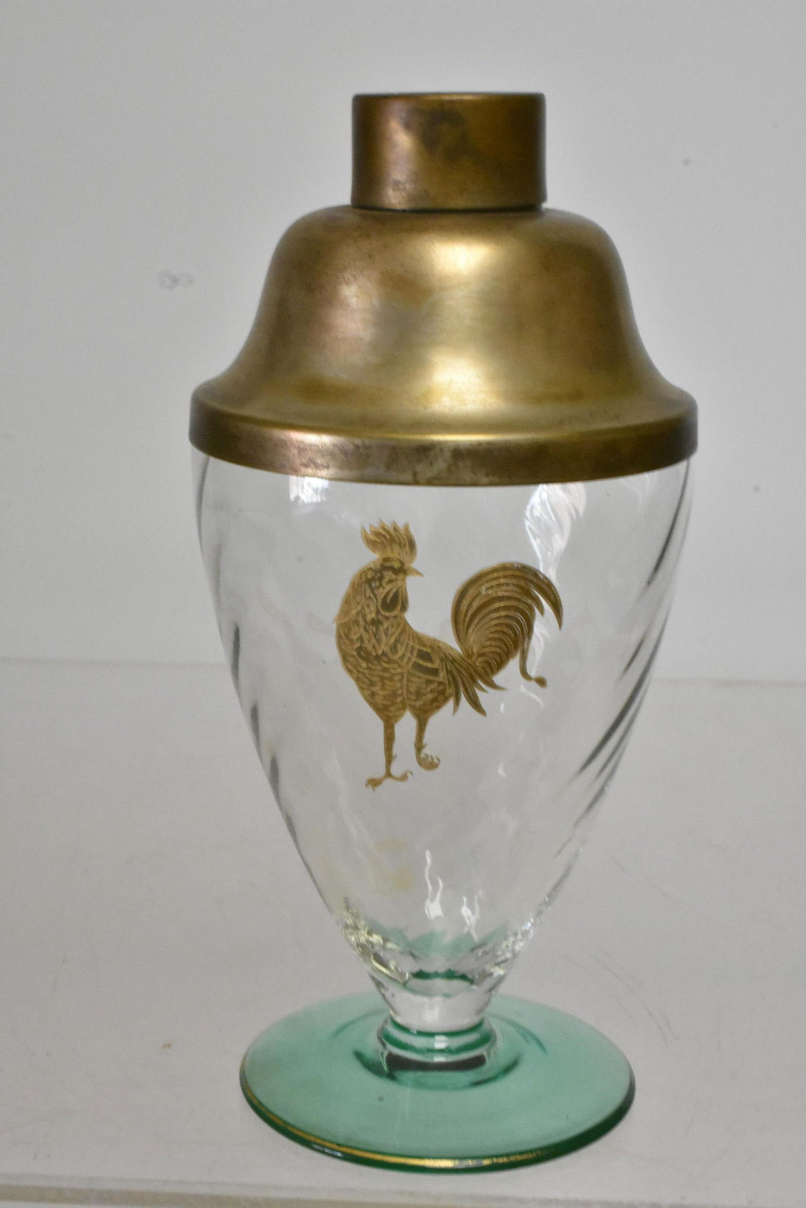 Glass Swirl Cocktail Shaker with Golden Rooster: Approximately 10"H. Swirled elegant glass body with green base. Applied rooster on side. Silver plated top. No seams present, free of chips and cracks. Shows wear to gold flash band at base.
