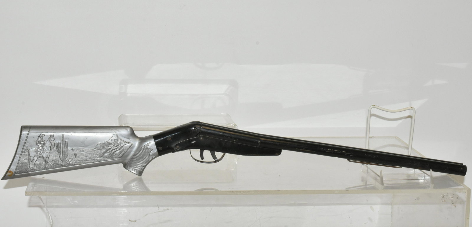 Mid 20th C Pop Gun Rifle: Approximately 30"L. Constructed of tin and plastic with cowboy motif. One trigger is functional. Clip from trigger mechanism is loose but present. Item sold as found.