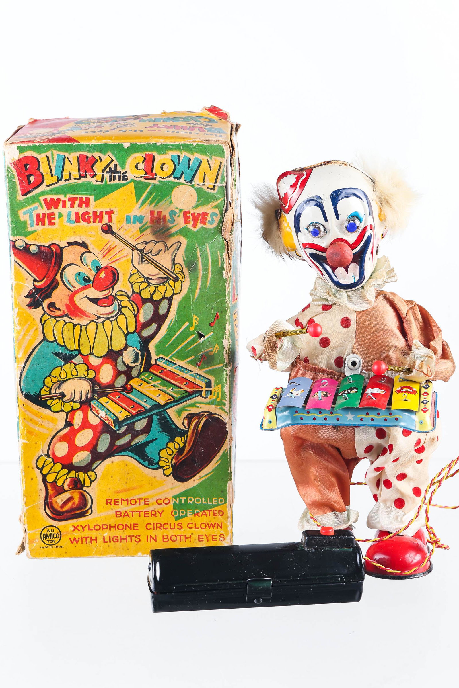 Amico Battery Operated Blinky the Clown in Box: Clown shows signs of age on clothing, measures 10 1/2" high with a tin litho head, xylophone, and shoes (paint is good). Actions include remote control light up eyes, arm, and head movement. Original