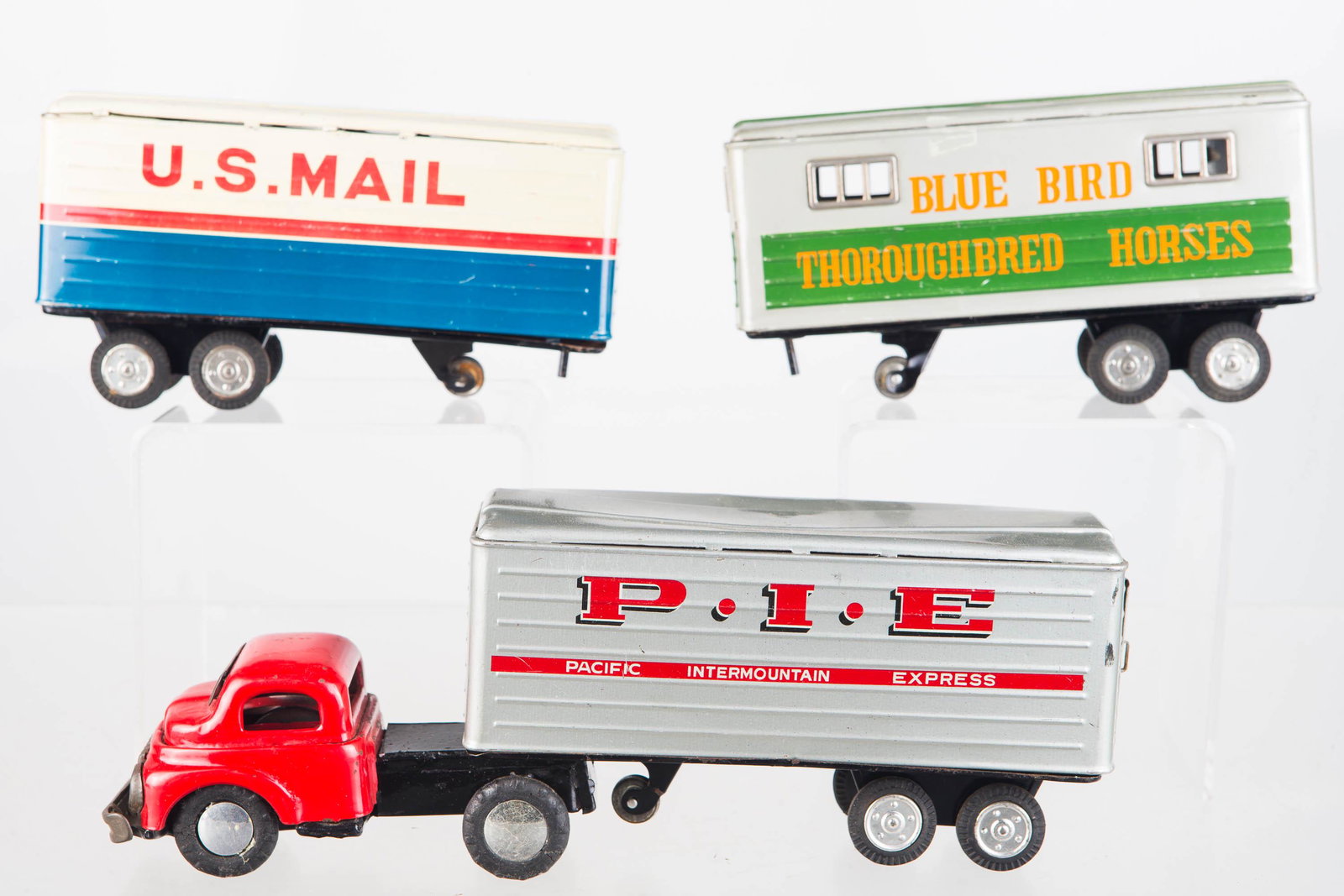 4 Piece Tractor Trailer Set: Tin Litho Japanese friction powered truck with one trailer attached measures 10 1/4" long. All pieces show signs of use including some denting on top of two trailers. Trailers read "U.S. Mail", "Blue 
