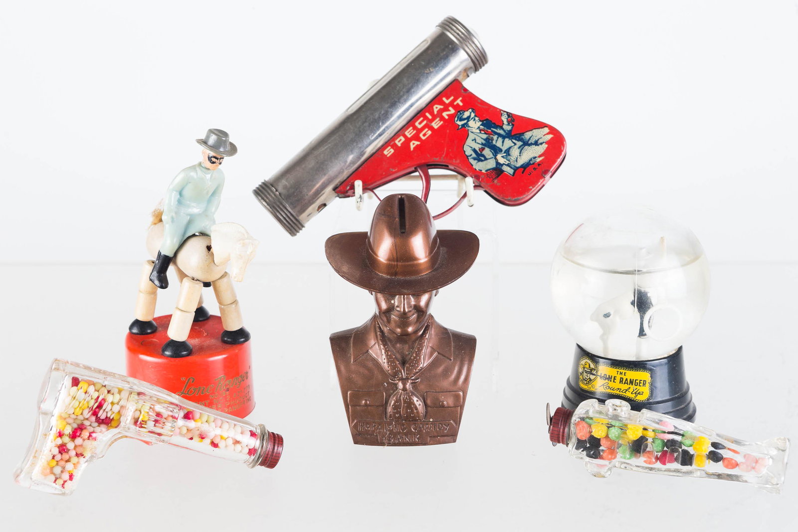 Western Hero and Candy Container Items: Lot includes an airplane and a pistol candy container, Lone Ranger snow globe with damage at base, Lone Ranger flex toy, a plastic Hoppy bank, and Special Agent flashlight pistol missing interior work
