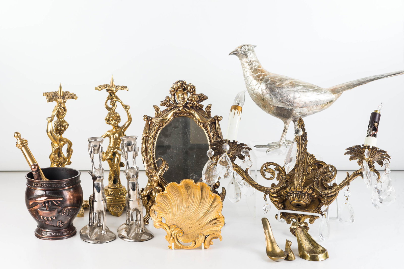 Figural Brass Candlesticks and Mixed Metalware: Lot includes a pair of putti brass candlesticks (11"H each), brass wall sconce with crystals, a pair of antelope candlesticks, a large decorative bird, putti wall mirror, a shell dish, and a metal mor